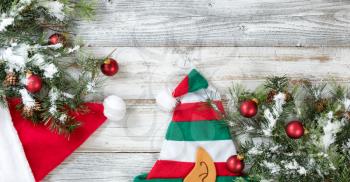 Snow covered Christmas Rough Fir Tree, Santa and elf hats on Weathered White Wooden Background