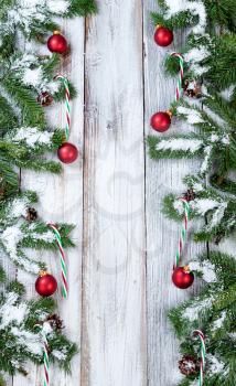 Snowy Christmas tree branches, candy canes and red ornaments forming vertical borders on rustic white wood