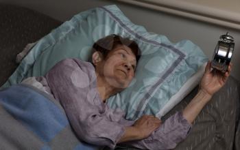 Restless senior woman glaring at her alarm clock during nighttime

