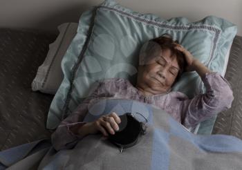 Restless senior woman holding alarm clock face down during nighttime