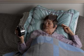 Restless senior woman staring at alarm clock during nighttime