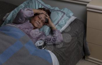 senior woman holding her forehead in pain during nighttime