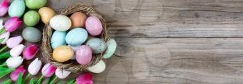 Tulips and colorful eggs in nest on rustic wooden boards for Easter Background 
