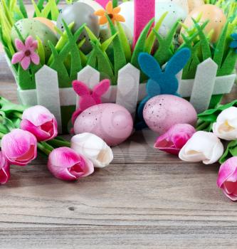 Front view of a carry basket filled with colorful eggs and pink tulips on weathered wooden boards for Easter background  