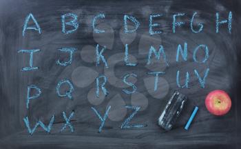 Alphabet blue letters with eraser and apple on blackboard 