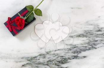 Single red rose on dark gift box with heart shaped card on marble stone background in flat lay view 
