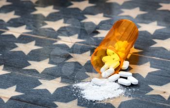 Front view of prescription bottle filled with generic opioid pain killer tablets on rustic USA flag in background for drug addiction concept in America  