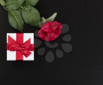Overhead view of a gift box and a single red rose on dark stone background