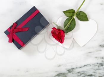 Single red rose on card with dark gift box on marble stone background in flat lay view 