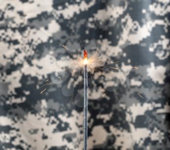 Glowing sparkler with camouflaged military uniform in background 