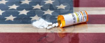 Bottle of prescription for Hydrocodone or generic opioid with crushed or whole pain killer tablets. Rustic USA flag in background for drug addiction concept in America  