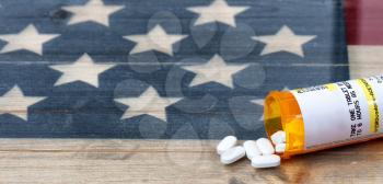 Prescription bottle of Hydrocodone or generic opioid pain killer tablets with rustic USA flag in background for drug addiction concept in America  
