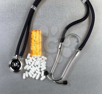 Oxycodone opioid tablets, bottle and stethoscope on stainless steel table in overhead view