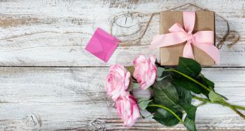 Pink roses and gift box for romantic celebrations on rustic white wood in flat lay view