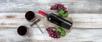 Overhead view of Red wine bottle with grapes, filled drinking glasses and corkscrew on weathered wooden boards