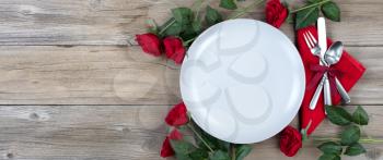 Holiday Dinner setting with red roses and silverware on rustic wood in flat lay view
