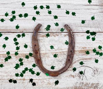 Close up view of a rusty horseshoe for St Patrick day with shiny clovers on weathered white wooden boards 