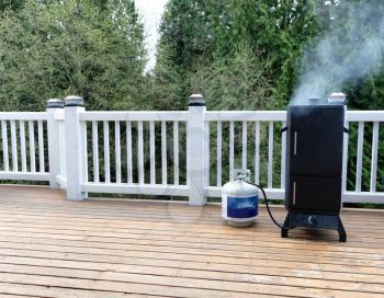 Gas smoker on cedar outdoor deck with woods in background