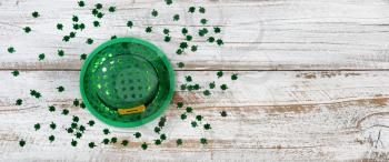 St Patrick day good luck hat with shiny clovers on rustic white wooden boards in overhead view 