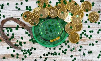 St Patrick good luck hat, green clovers and horseshoe with shiny gold coins on rustic white wooden boards 