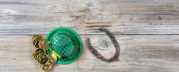Lucky green hat, horseshoe and gold coins for St Patrick on rustic wooden boards in overhead view 