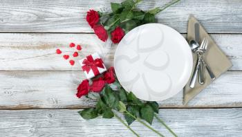 Valentine dinner setting with gift, red roses and heart shapes on rustic table 
