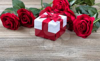 Gift box with red roses in background on weathered wooden background in close up view  