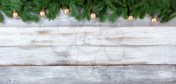 Top border of Christmas evergreen branches and Golden ornaments on white vintage wood