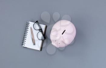 Piggy Bank and traditional writing stationery on gray desktop 