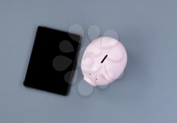 Piggy Bank and modern portable technology on gray desktop 