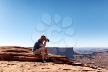 Man sitting down taking photos of Grand Canyon during summer day 