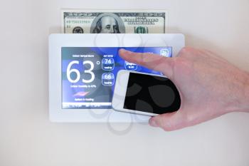 Male hand holding smart phone to operate heating or cooling of thermostat for home energy savings