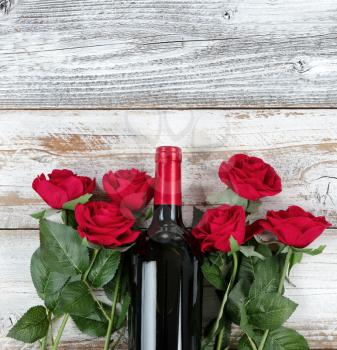 Romantic Valentines Day celebration with red wine and roses forming bottom border on white rustic wood 