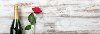 Anniversary background with red rose and champagne on white rustic wood 