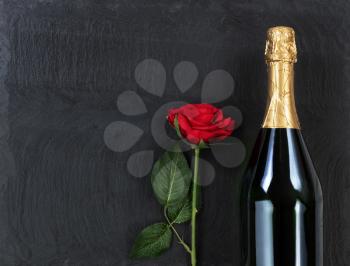 Anniversary background with red rose and champagne on natural black slate stone 