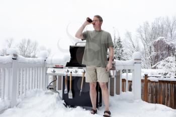 Mature man drinking beer while preparing to barbecue during winter season  