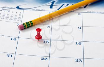 Red pushpin on day of April 15 of calendar for tax income due date reminder with pencil in background 