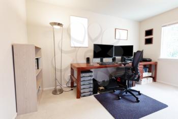 Comfortable computer chair at large work table with computer monitors and other technology equipment in bright home office interior  