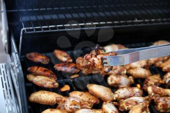 Close up of an open barbecue grill cooking chicken wings with tong holding a single piece  