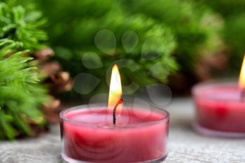Single traditional glowing Christmas holiday candle with evergreen branches in background 