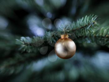 Traditional golden single Christmas ornament hanging on artificial tree 