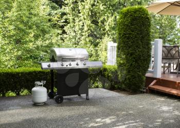 Barbeque cooker on concrete outdoor patio with woods and home deck in background