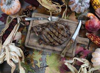 Freshly grilled steak with utensils on table decorated with seasonal autumn vegetables 