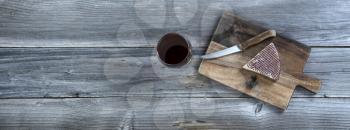 Fresh cheese wedge on cutting board with red wine in a glass on rustic wooden table 