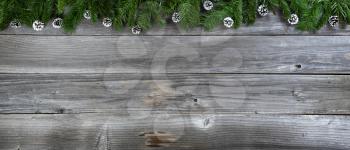 Merry Christmas and Happy New Year concept with pine cone ornaments inside of fir branches on rustic wooden boards 