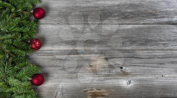 Merry Christmas and Happy New Year concept consisting of fir branches and red ball ornaments on left side of rustic wooden boards