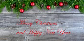 Overhead view of real fir Christmas tree branches and red ornaments on weathered wood  with holiday message