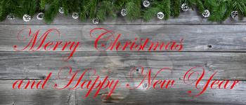 Merry Christmas and Happy New Year concept with pine cone ornaments inside of fir branches on rustic wooden boards plus text message 