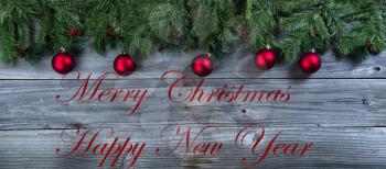 Christmas rustic natural wooden background with evergreen branches and red ball ornaments plus text message 