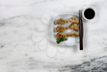 Plate filled with freshly fried Chinese dumplings and dipping sauce on marble top table 
